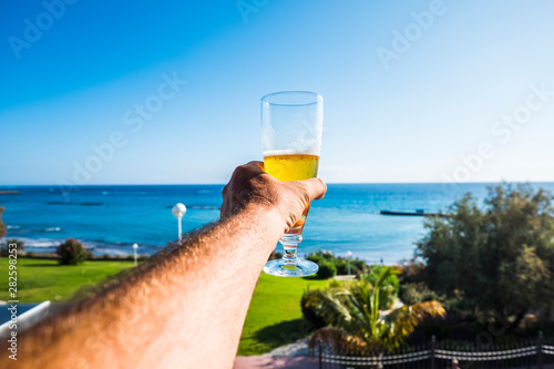 Close up of man hand with pint of beer enjoying the summer holiday beautiful torpical beach vacation -  blue sky and ocean in background photo