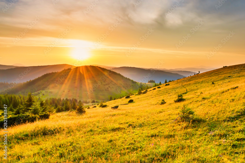 Fotobehang Oranje Sunset in the mountains with forest, green grass and big shining sun on dramatic sky #282598847
