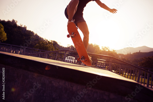 Skateboarder doing ollie at sunrise skatepark ramp