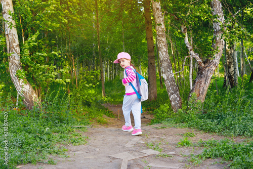 Cute child girl goes to school alone through a path in the forest. Back to school. © NATALYA