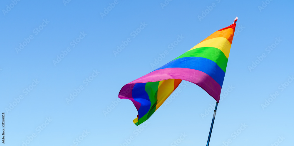 Gay rainbow flag waving in the wind in a clear blue sky Gay rainbow flag waving in the wind in a clear blue sky