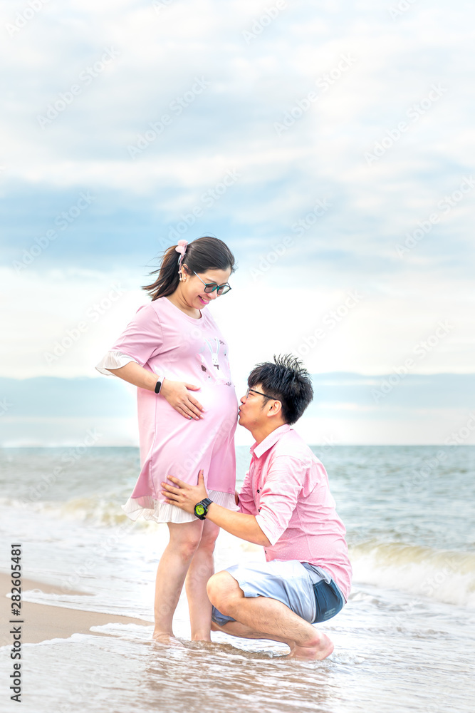 Happy moments, Asian husbands are kissing the pregnant mothers stomach on the beach.
