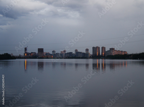 The modern city center is reflected in the water of the lake. Glowing buildings in the evening.
