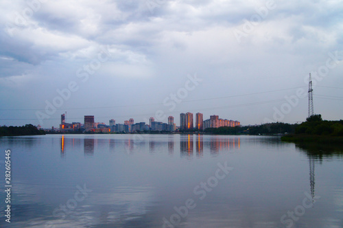 The modern city center is reflected in the water of the lake. Glowing buildings in the evening.