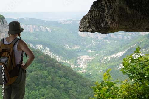 a girl-traveler in a backpack looks into the distance from a cliff on the ruins of a medieval fortified city