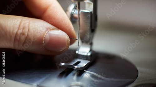 Close up view of presser foot. Tailor skillful fingers pulling thread in needle's loop on modern manufacturing machine for beginning stitching. Steel needle loop and presser foot. Blurred background