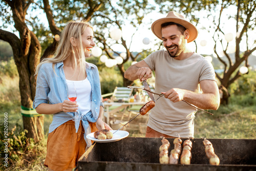 Couple of friends having barbecue, cooking food in the beautiful garden during a festive lunch on a summer aftenoon photo