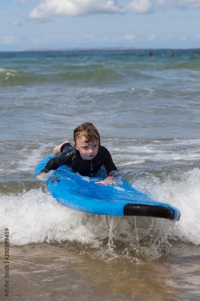 Little boy learning to surf at the beach, getting up on surfboard for the first time, west coast of Ireland Little boy learning to surf at the beach, getting up on surfboard for the first time, west coast of Ireland