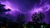 bright flashes of lightning during night thunderstorms, silhouettes of trees and houses against the dark blue sky