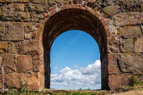 Summer view through an old medieval stone wall arched gate at Varberg Fortress in Sweden with blue cloudy sky in the background.