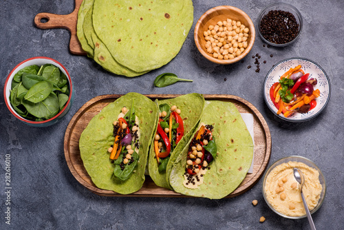 Vegan green tortilla flatbreads or tacos for healthy snack with cheakpeas, hummus, grilled vegetables, beluga lentils and spinach