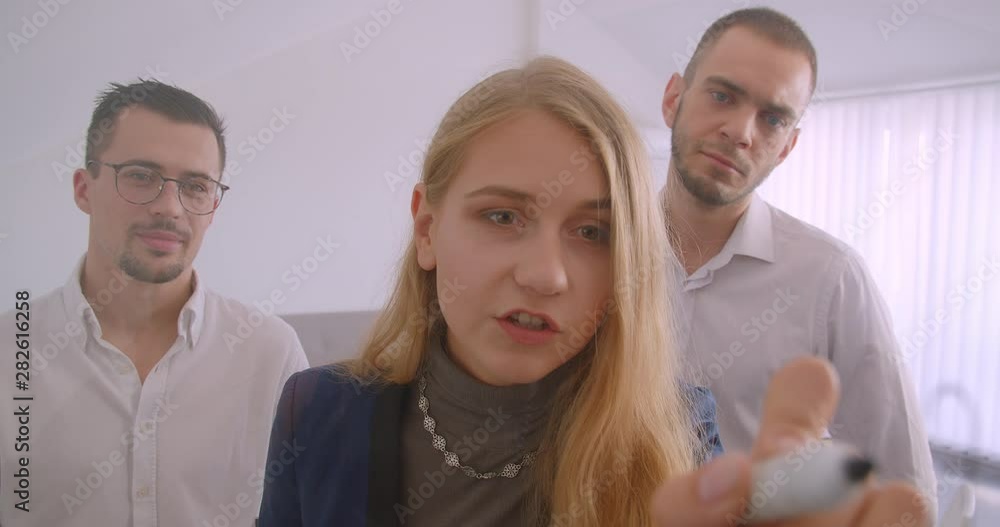 Portrait of three collleagues working together in the office indoors. Successful businesswoman brainstorming ideas on the screen while two men are observing Portrait of three collleagues working together in the office indoors. Successful businesswoman brainstorming ideas on the screen while two men are observing