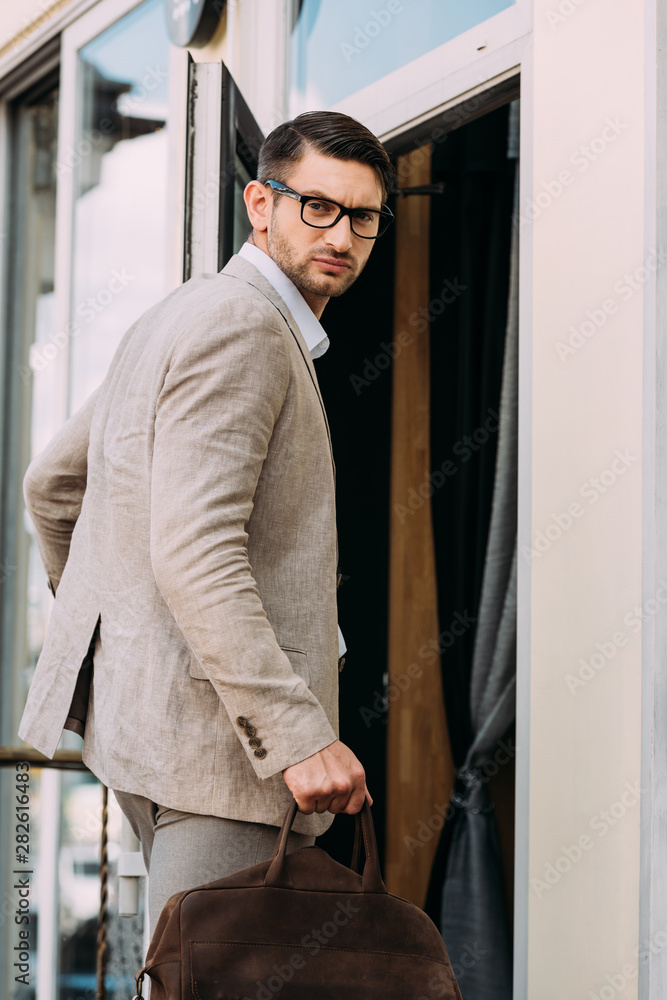 serious businessman in glasses holding leather bag and looking at camera serious businessman in glasses holding leather bag and looking at camera