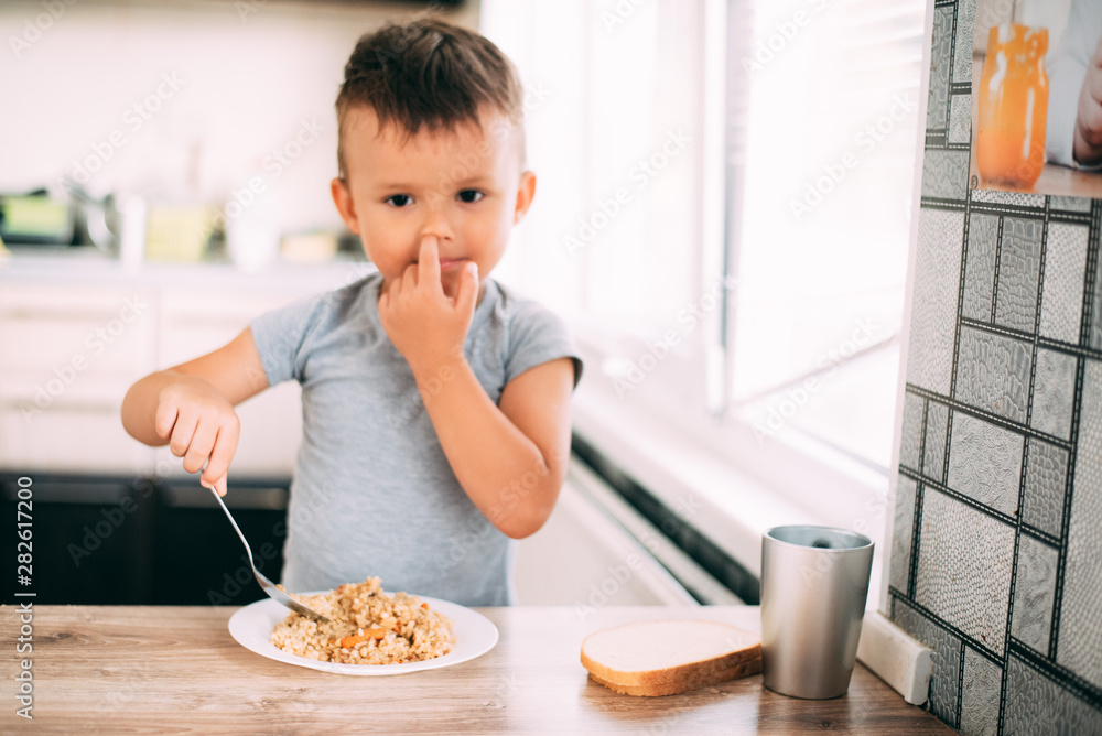 The child eats pilaf with carrots in the kitchen during the day The child eats pilaf with carrots in the kitchen during the day