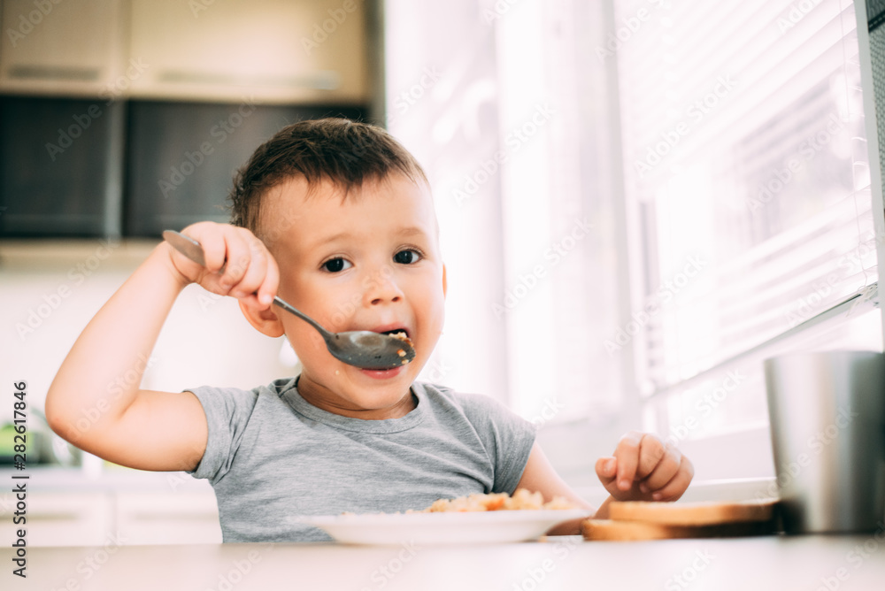 The child eats pilaf with carrots in the kitchen during the day The child eats pilaf with carrots in the kitchen during the day