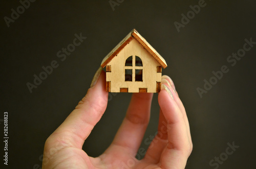Wooden toy house model in woman hand on black background front view  with a copyspace