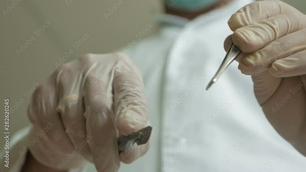close-up in focus surgeon's hands holding a surgical instrument approaching the camera out of focus in the background out of focus doctor in medical uniform in bandage surgery scalpel in doctor’s hand close-up in focus surgeon's hands holding a surgical instrument approaching the camera out of focus in the background out of focus doctor in medical uniform in bandage surgery scalpel in doctor’s hand