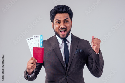 happy indian student male bearded wearing stylish classic suit holding passport airline ticket white studio background . lifestyle summer trip concept