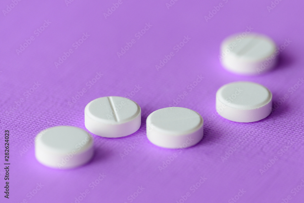 White tablets scattered on a purple background close up White tablets scattered on a purple background close up