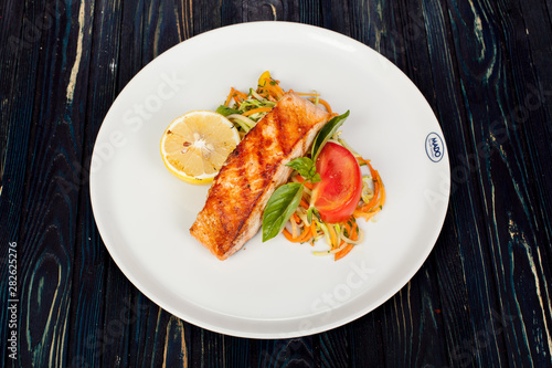 appetizing fried fish, beautifully laid out with greens and vegetables on a dish, for designer solutions in cooking