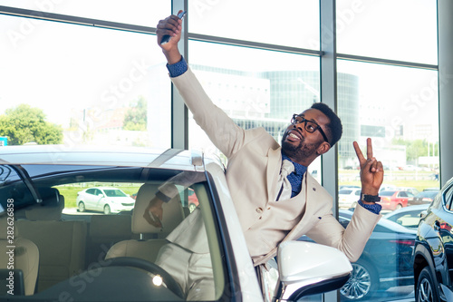 Wallpaper Mural portrait of african american car sales consultant in showroom and making selfie photo on camera smartphone Torontodigital.ca