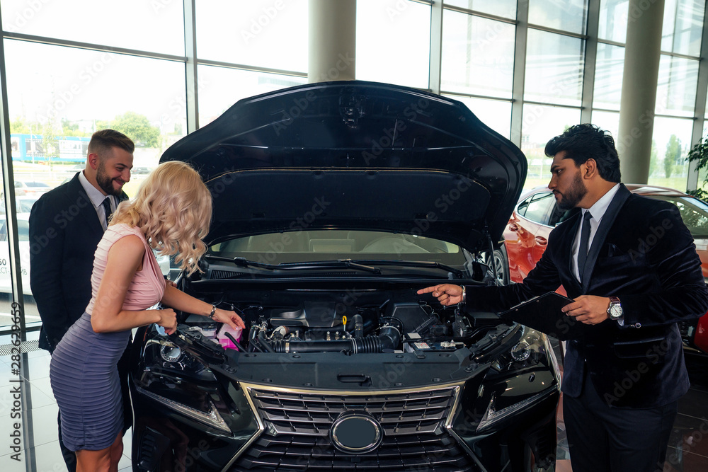 handsome indian salesman showing luxury auto for rich family buyers at modern showroom.husband and wife choosing car handsome indian salesman showing luxury auto for rich family buyers at modern showroom.husband and wife choosing car