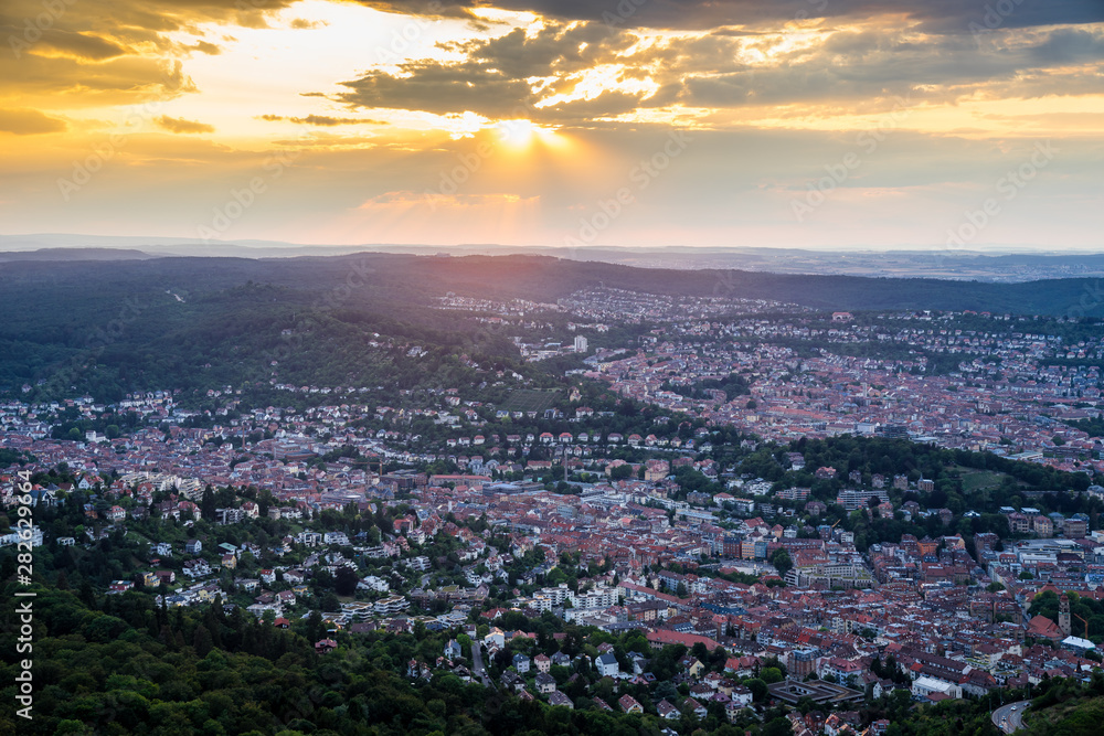 Germany, Endless aerial view above roofs and houses of city stuttgart in basin surrounded by green forest at sunset