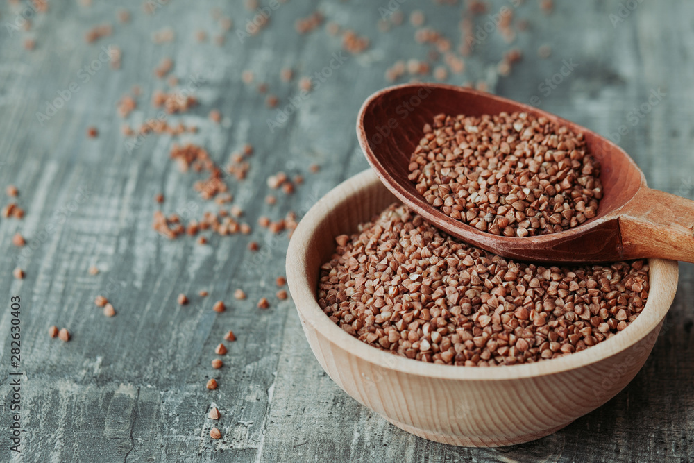 Close-up photo of dry buckwheat in a wooden plate with a wooden spoon. Free space for text mockup Close-up photo of dry buckwheat in a wooden plate with a wooden spoon. Free space for text mockup