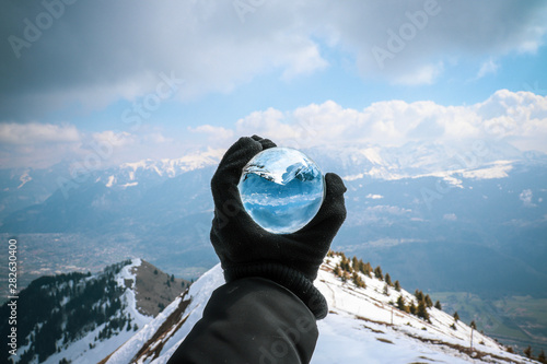 Main tenant une boule de verre face à une montagne