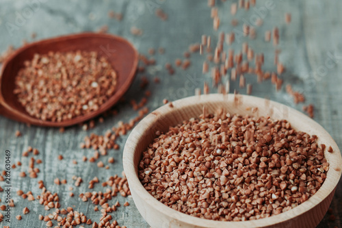 Close-up photo of dry  buckwheat in a wooden plate with a wooden spoon. Free space for text mockup