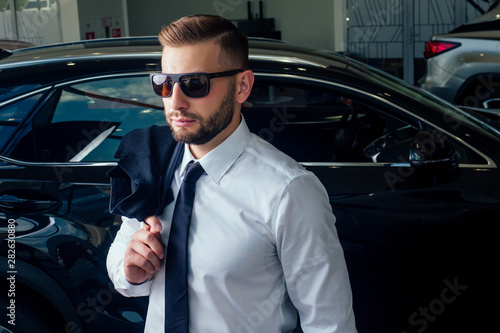 Smiling well-dressed man posing near a car at showroom