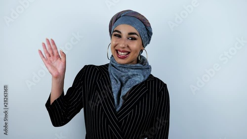 young beautiful arabic woman waving her hand and generously smiling on isolated white background photo