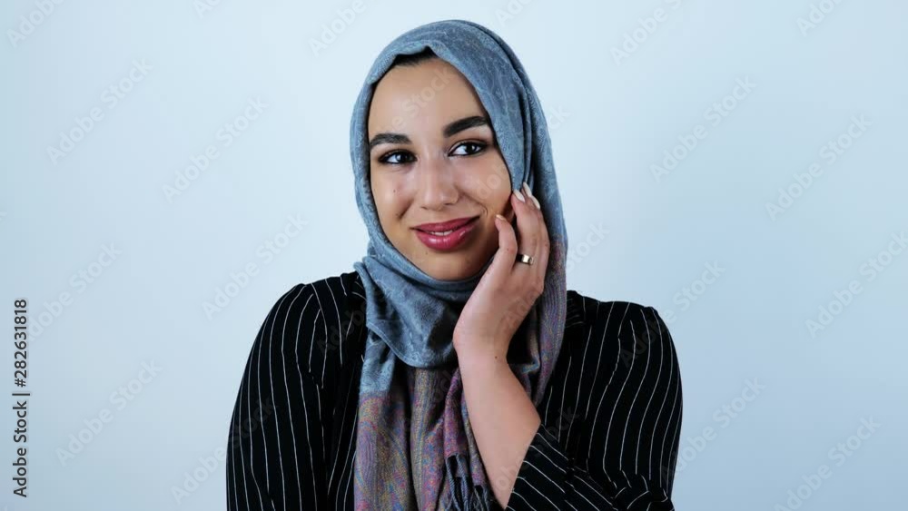 young beautiful arabic woman smiling feeling a bit shy touching her face with her hand on isolated white background young beautiful arabic woman smiling feeling a bit shy touching her face with her hand on isolated white background
