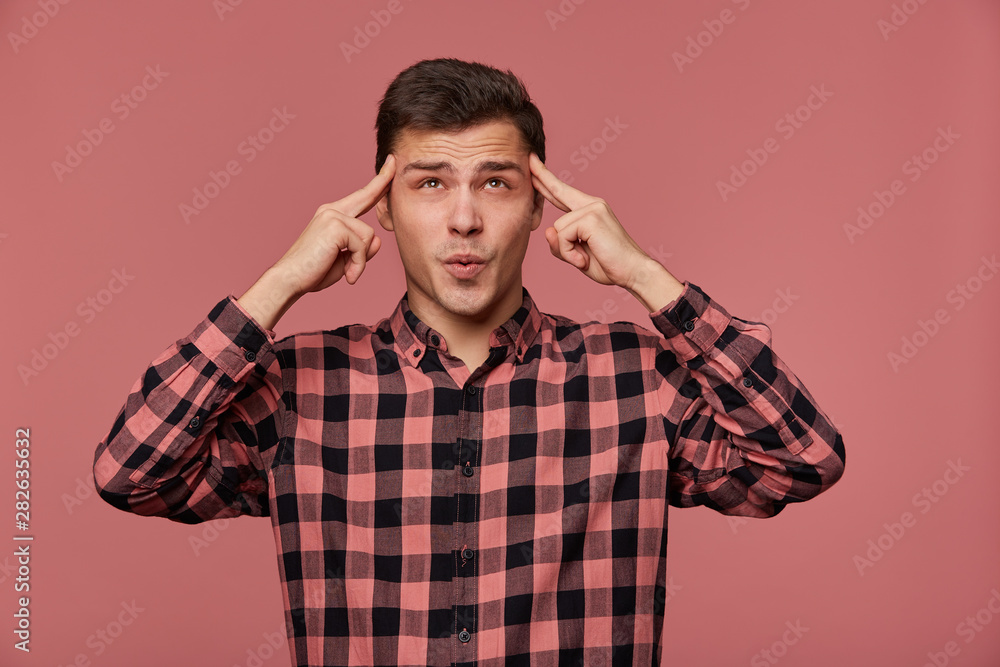 Portrait of young attractive man in checkered shirt, looks at the camera, stands over pink background and shows headshot gesture. Portrait of young attractive man in checkered shirt, looks at the camera, stands over pink background and shows headshot gesture.
