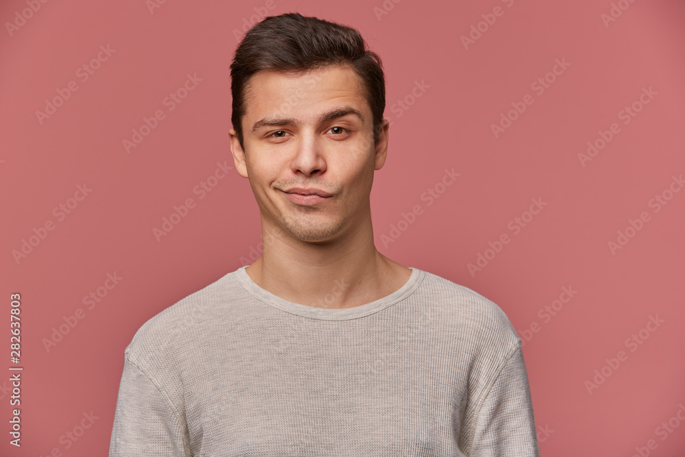 Portrait of handsome young man with raised eyebrow in disapproval, wears in blank t-shirt, looks at the camera with a grin and doubts, stands over pink background. Portrait of handsome young man with raised eyebrow in disapproval, wears in blank t-shirt, looks at the camera with a grin and doubts, stands over pink background.