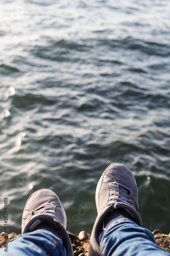 man's feet waring sneakers and blue jeans at sea 