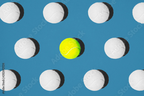 Creative composition made with yellow tennis ball and white balls on blue background.