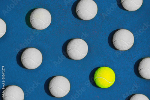Creative composition made with yellow tennis ball and white balls on blue background.