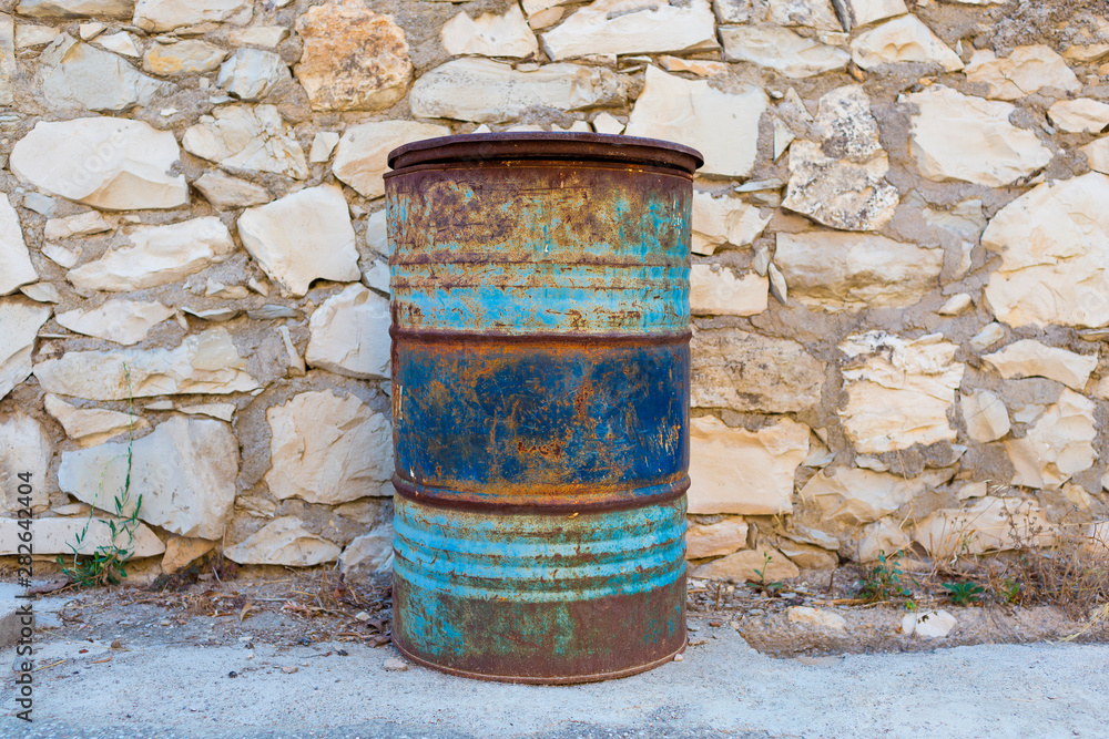 Obraz premium Big rusty blue barrel stand near a stone wall in the backyard.