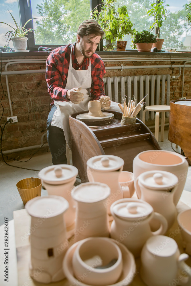 Young successful potter in workwear working over new clay item in his own workshop Young successful potter in workwear working over new clay item in his own workshop