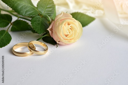 Wedding background, greeting card with two golden rings, rose and white dress, space for text.