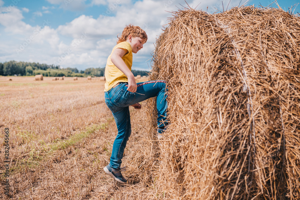 A British red-haired boy climbs a haystack in a field A British red-haired boy climbs a haystack in a field