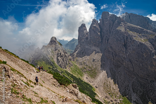 Some hikers go along an impassable rocky path, in view of the towers and peaks of the Friulian Dolomites, in Italy.