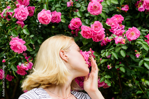 Spring and summer. Perfume and cosmetics. Woman in front of blooming roses bush. Blossom of wild roses. Secret garden concept. Aroma of roses. Girl adorable blonde sniffing fragrance of pink bloom