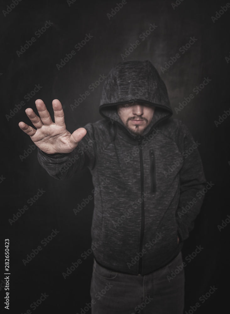 Unknown man in hood pointing by hand on dark. Focus on hand