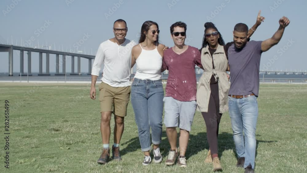 Group of smiling friends hugging while strolling on meadow. Happy young people having fun together. Friendship concept