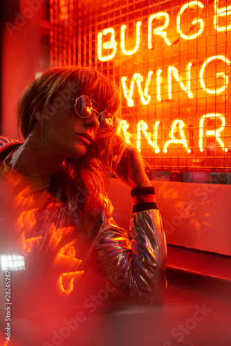 Portrait of woman with silver jacket and sunglasses in neon lights