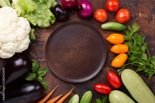 Assorted raw organic vegetables and empty plate on dark stone background Harvest time Vegetarian eating and dieting concept Top view Copy space