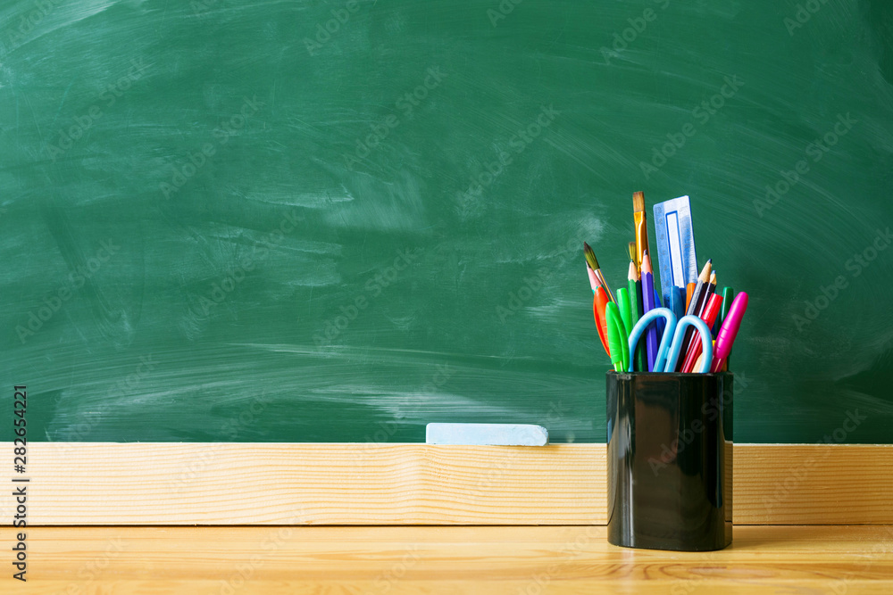 Back to school. Pens, pencils, brushes in a glass against the background of a green blackboard. School background with space for your text Back to school. Pens, pencils, brushes in a glass against the background of a green blackboard. School background with space for your text
