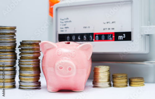 Piggy bank with coins near the natural gas meter at home. Energy saving or cost of natural gas for heating a house concept image. Symbolic image of a payment for heating in winter. Selective focus photo